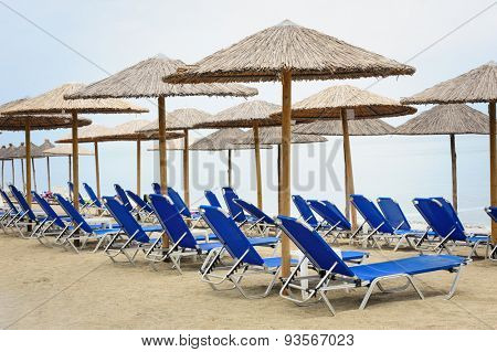 Rows of reed umbrellas and blue deck chair on the sea beach 