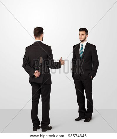 Two opposing businessman shake hands, one of them hiding a weapon behind his back