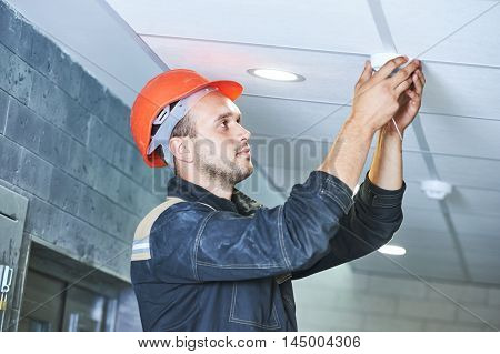 worker installing smoke detector on the ceiling