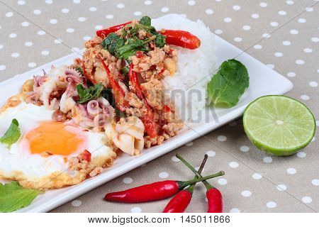 Rice topped with stirred  minced-pork ,squid ,basil and fried egg(sunny up) on brown napery. Selective focus.