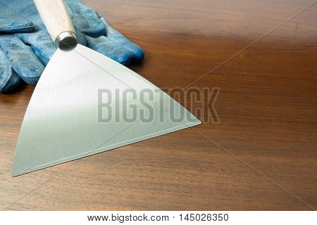 paint scraper with wood handle and working gloves.