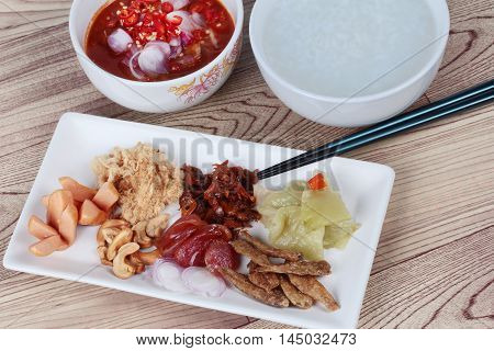 Rice gruel and  side dish  on wood. (Dried shredded pork,Chinese sausage,crispy fish,sausage, fried baby clams,sliced red onion,pickle Chinese cabbage ,Spicy sardine salad and shallots )