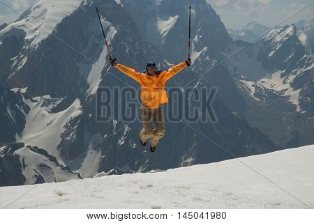 Mountain travel. Woman jumps and lifts her arms in victory. Woman dressed in orange windbreaker.
