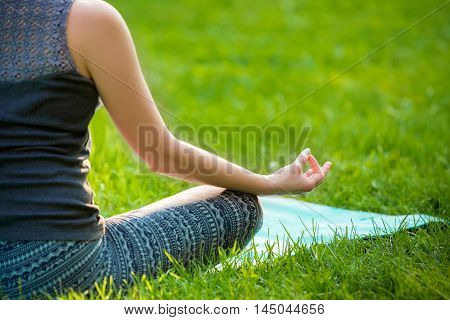 Meditating woman in meditation in city park in yoga pose. Girl relaxing with serene relaxed expression outside in summer. Beautiful young Caucasian female model. Close up