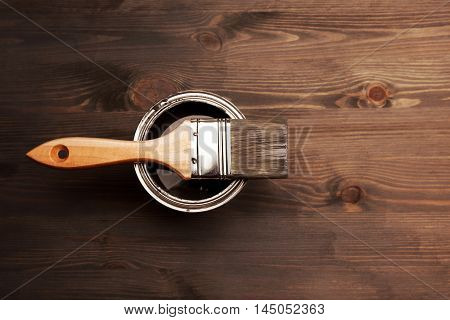 Paintbrush and a opened can of grey paint on fresh painted wooden surface