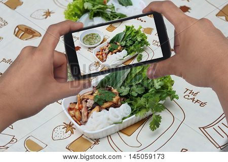 Friend using smart-phone to take photo roll noddle served with fried tofu and mixed vegetables for share to social network.