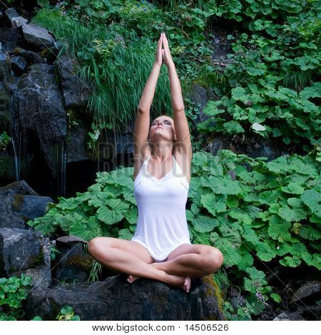 Beautiful young Woman doing Yoga im Lotussitz in der Nähe von Wasserfall und grüne Blätter