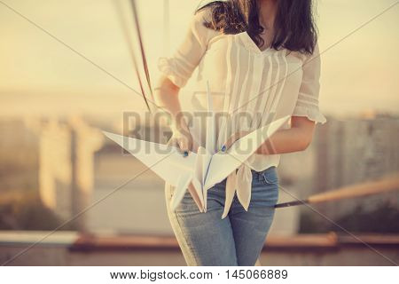 Beautiful young girl at the roof with origami paper crane in hands. Vintage tinted selective focus.