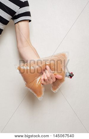 hand holding plastic bag with tap full of apple juice, stucco wall background