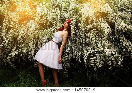 Beautiful girl (25 years old) in white wedding dress on a background of spirea bushes with lots of small white flowers