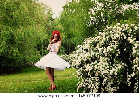 Beautiful girl (25 years old) in white wedding dress on a background of spirea bushes with lots of small white flowers