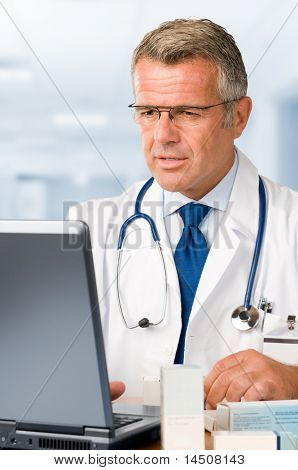 薬の処方箋彼の診療所のオフィスでのノート パソコンで作業して成熟した医師