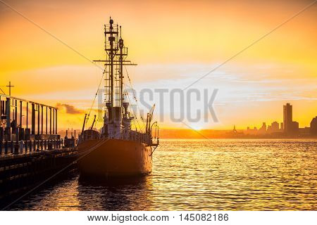 Cargo ship in the harbor at commercial port at sunset time. Sun is going down against beautiful sky at the dock with mooring vessel.