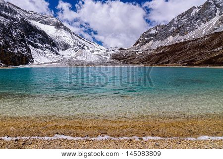 Blue green Milk lake in the snow mountains with clouds and sky at Yading Nature Reserve, China.