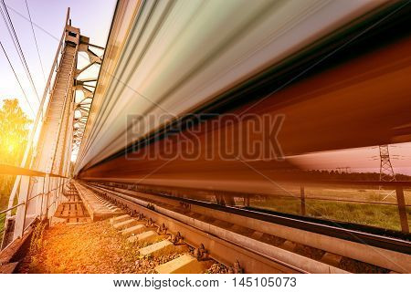 Highspeed train moves fast on the bridge at sunset.