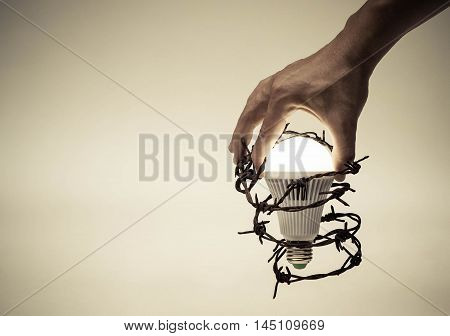 Hand trying to catch a turned on LED light bulb with barbed wire / Something stops new idea / Freedom of thought and idea expression