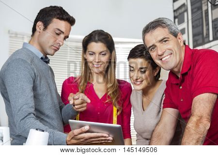 Confident Tailor Standing With Colleagues Using Tablet Computer