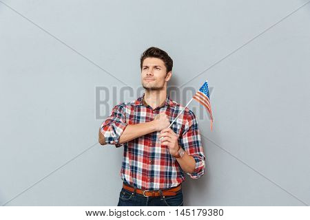 Patriotic proud young man standing and holding flag of USA over grey background