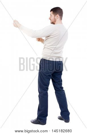 back view of standing man pulling a rope from the top or cling to something. bearded man in a white warm sweater pulls the rope side.