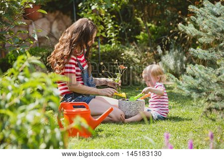 Pregnant woman with little daughter in the summer orchard cearing flower.