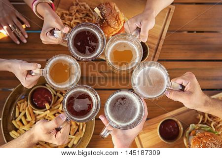 Group of friends drinking beer and eating snacks on wooden background