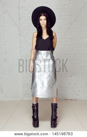 Confident girl holding all in her hands and control of all. Model in the studio posing to the photograther with black hat near grey brick wall. She is sad