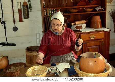 Old Salem North Carolina - April 21 2016: Docent in traditional Moravian clothing sewing at a kitchen table at the 1771 Miksch House