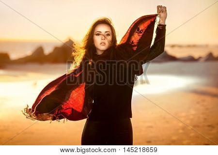 Beautiful fashion woman posing on the ocean beach wearing autumn clothes at sunset time