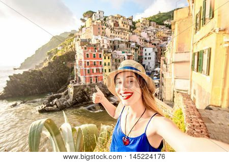 Young female traveler making selfie photo on the old coastal town in Riomaggiore in Italy. Happy vacations in Italy