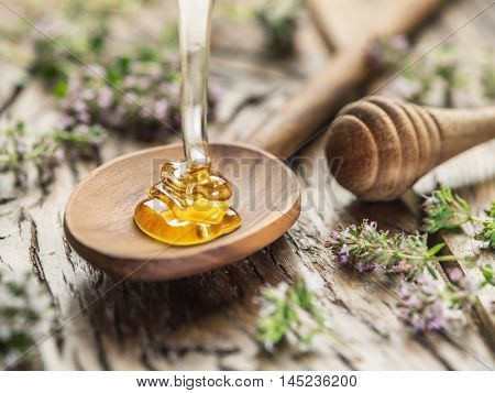 Herbal honey pouring into the wooden spoon. Spoon is on old wooden table surrounded with levender flowers.