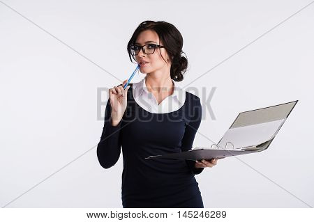 Young Caucasian woman wearing a dark blue dresst and and a white shirt, holding a ring binder folder and pen. Isolated on light background