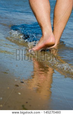 man walking barefoot on seacoast at bright sunny day