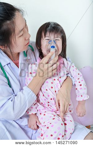 Closeup asian child having respiratory illness helped by doctor with inhaler. Pediatrician take care girl with asthma problems making inhalation with mask at hospital. child was bronchitis and crying.