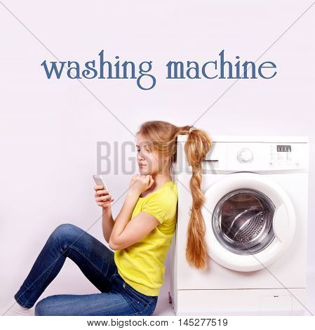 Beautiful happy girl with long hair and a cell phone in hand sits leaning on the washing machine on a white background