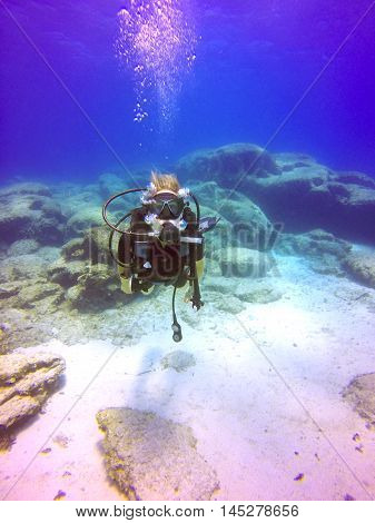 A young scuba diver lady swimming underwater. View of the scuba diver gear fins mask regulator bcd and bubbles maintaing buoyancy in the deep blue sea of Protaras Cyprus.
