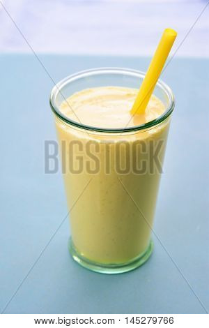 Mango lassi in glass with straw. Mango smoothie made with mango and yogurt yoghurt. Selective focus. Angle view.