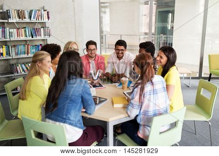 education, high school, learning, people and technology concept - group of international students sitting at table with tablet pc computers and books and talking at university
