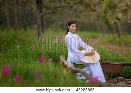Beautiful vietnamese girl in traditional dress (ao dai) in a park with beautiful pink flower background