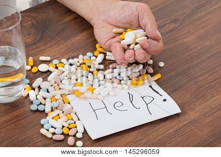 Person Holding Pills In Hand With Help Text On Paper
