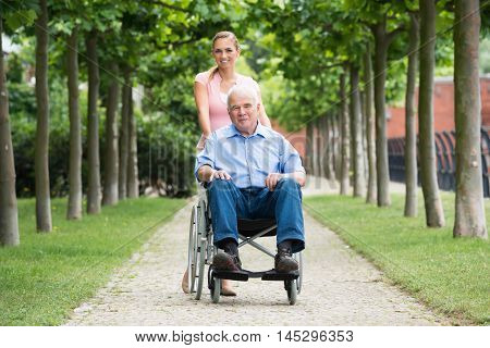 Happy Young Woman With Her Old Senior Father On Wheelchair In Park