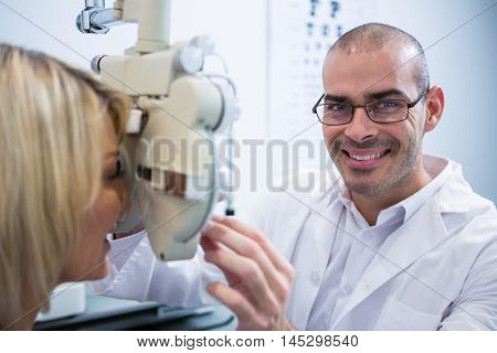 Smiling optometrist examining female patient on phoropter in ophthalmology clinic