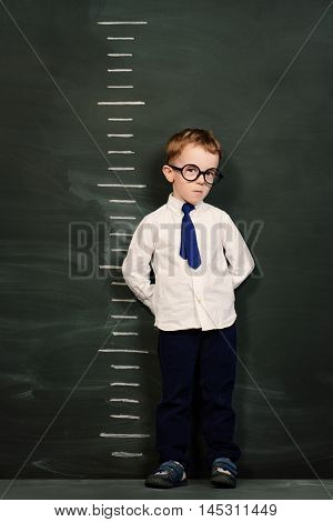 Four year old boy in white shirt and a tie standing by a stadiometer, drawn on a blackboard. Education.