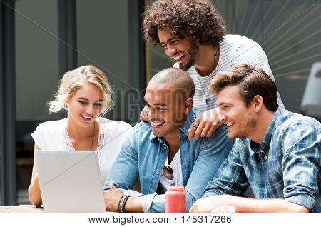 Happy smiling guys and girl studying with laptop at cafe. Group of laughing friends studying on a computer together in a summer day. Happy students enjoying together and watching a monitor of laptop.