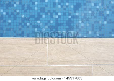 Close focus of edge of artificial wood floor near swimming pool with moving blue water