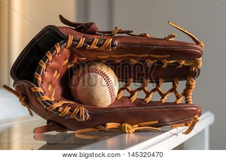 Close-up of a used baseball ball inside brown leather baseball glove on plain grey background.