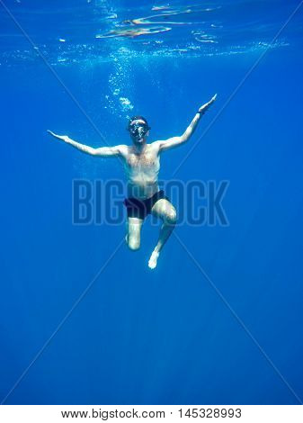 Portrait of a young causasian man meditating in the lotus position underwater. Submerged under water free diving crossed legs wearing a mask and blowing bubbles.