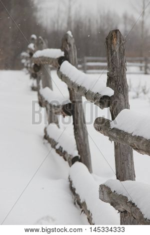 old rough rustic fence, made of logs, covered with snow