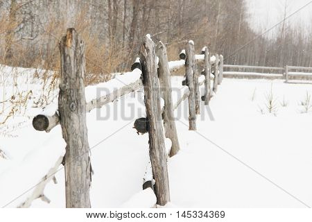 old rough rustic fence, made of logs, covered with snow
