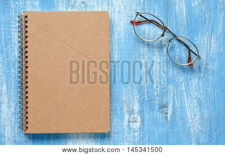 Brown notebook with glasses on blue wooden floor.