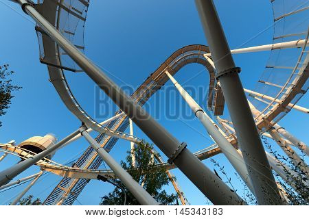 Bottom view of a white roller coaster on a clear blue sky at sunset